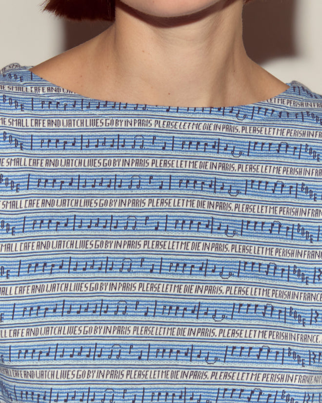 Close-up of the Lyric Long Sleeve in blue, featuring black musical notes, jacquard stripes, and repeated text: "PLEASE LET ME DIE IN PARIS.