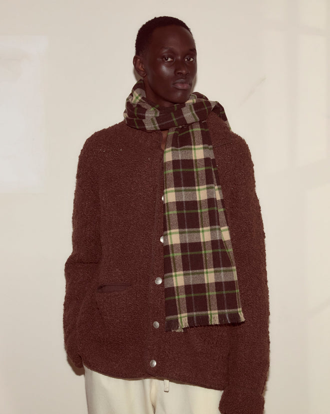 Person wearing a brown textured jacket, cream pants, and the Woodcrest Scarf from Camp Onibar, standing against a light wall.