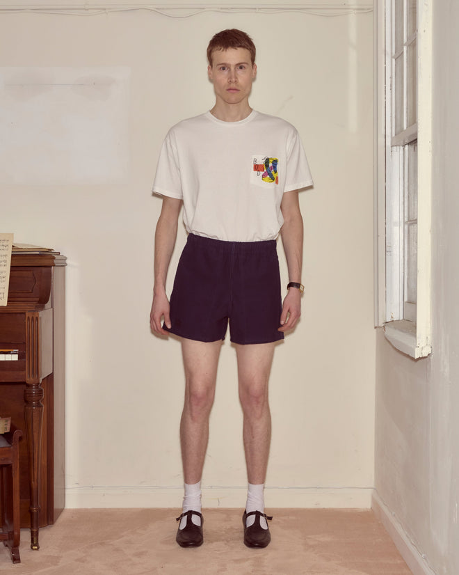 A man stands indoors wearing a white T-shirt, Field Shorts - Navy, white socks, and black shoes.