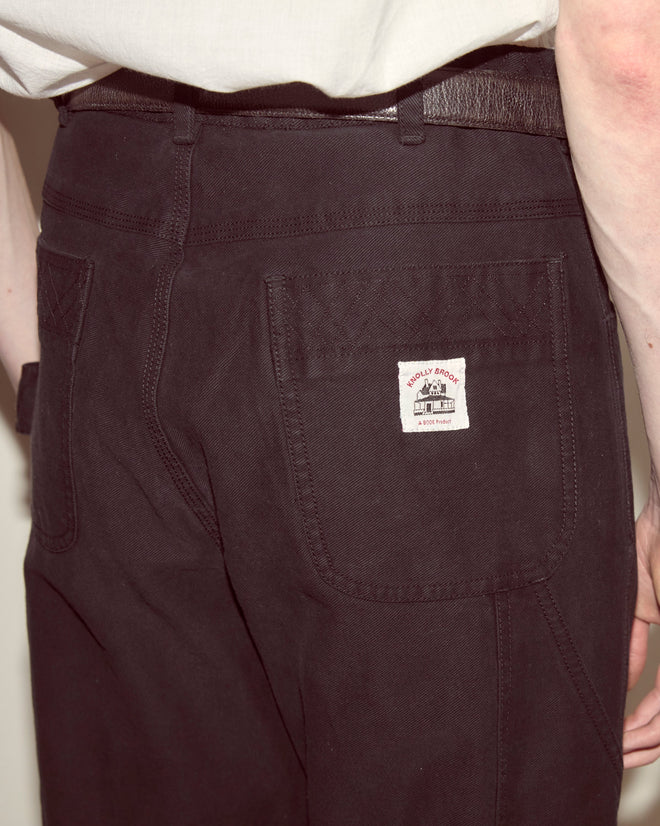 A person wears black Embroidered Denim Knolly Brook Trousers with a visible “WALLY BROWN” back pocket label, made from 100% cotton, and a white shirt tucked in.