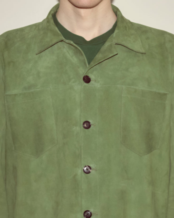A person wears the Suede Overshirt - Green in a workwear silhouette over a green shirt, shown from shoulders to chest.