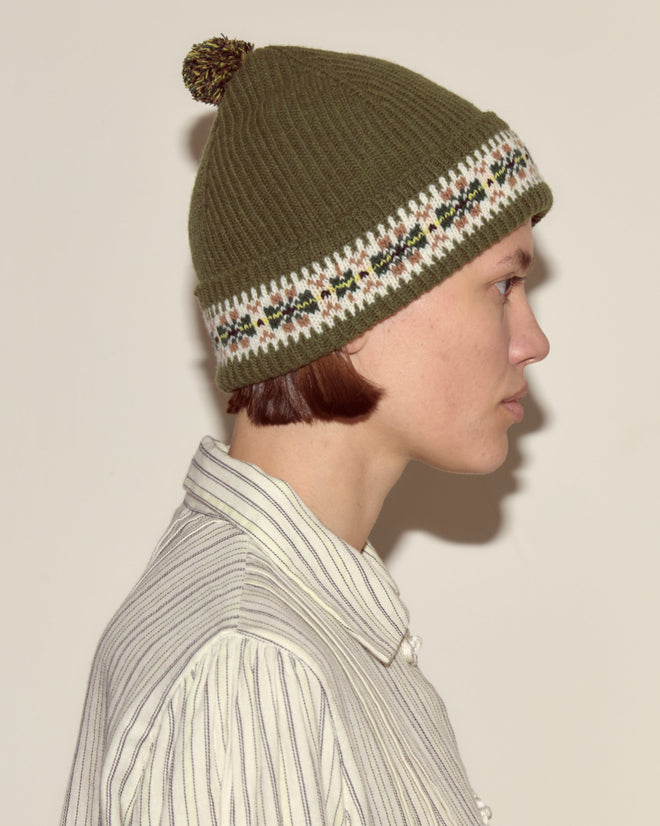 Person in profile wears the Moritz Hat in olive green merino wool with a striped shirt against a plain background, highlighting understated luxury accessories.