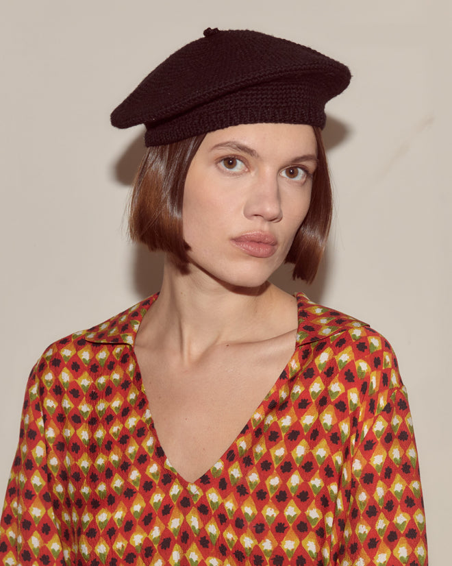 Woman with a bob haircut wears a black Crochet Beret and a patterned red, yellow, and black top, facing forward.