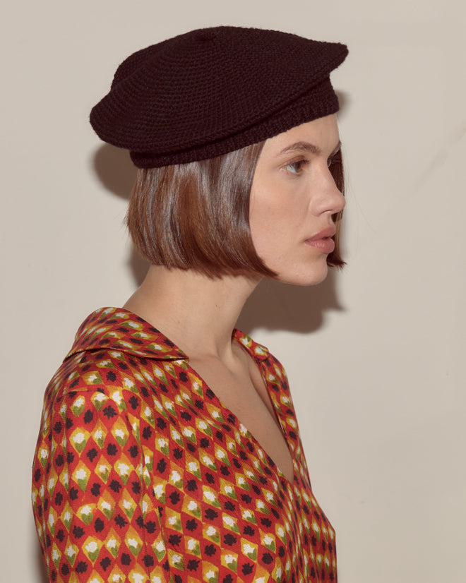 Woman in a patterned shirt and black crochet beret, with short brown hair, looking to the right.