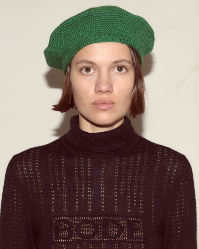 Person wearing a green Crochet Beret and a black knit sweater, looking directly at the camera against a plain background, showcases understated style with vintage accessories.